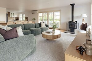 A modern living room with a sectional sofa, a round wooden coffee table, and a black wood-burning stove.