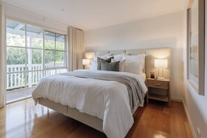 Un dormitorio con una cama grande, dos mesitas de noche, un ventanal con cortinas y vistas al exterior.