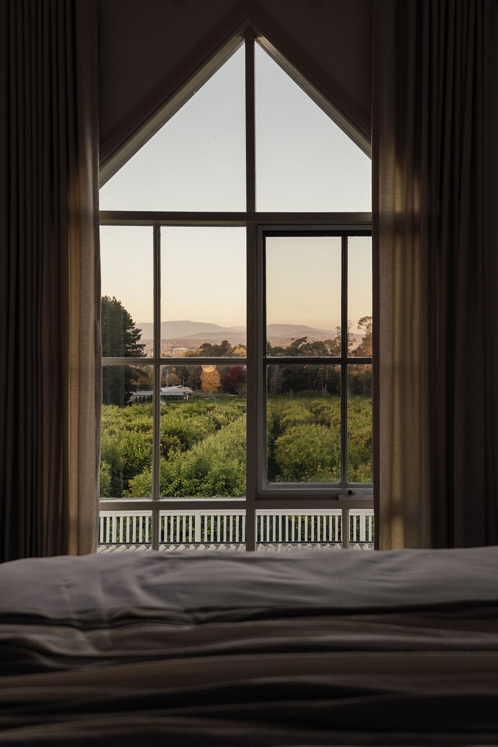 Une chambre avec une grande fenêtre donnant sur un jardin et des collines lointaines.