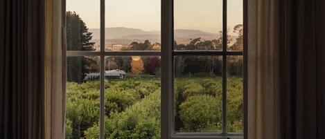 A bedroom with a large window overlooking a garden and distant hills.