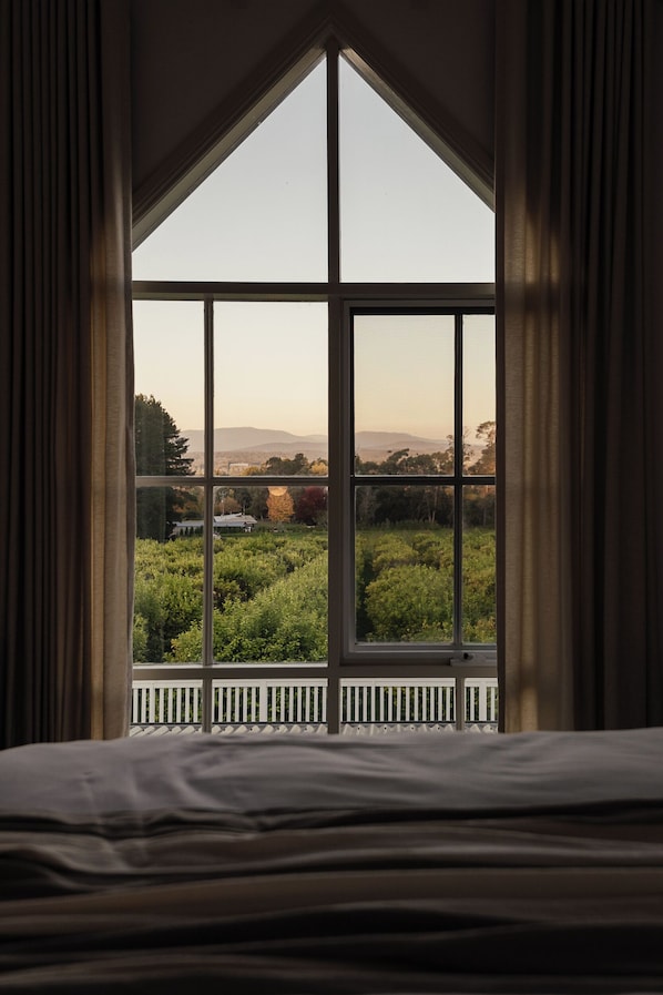 A bedroom with a large window overlooking a garden and distant hills.
