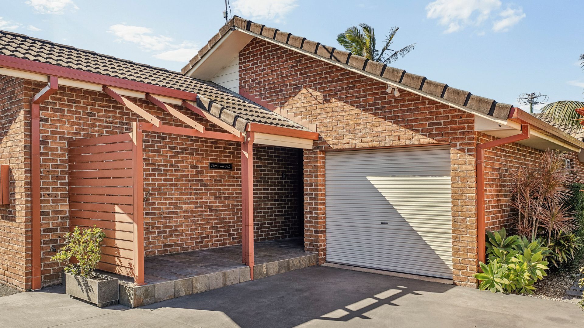 Un immeuble résidentiel avec une façade en briques, un garage doté d’une porte à enroulement et un petit espace porche.
