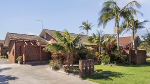 A residential property with a brick exterior, a tiled roof, and a well-maintained garden with palm trees and shrubs.