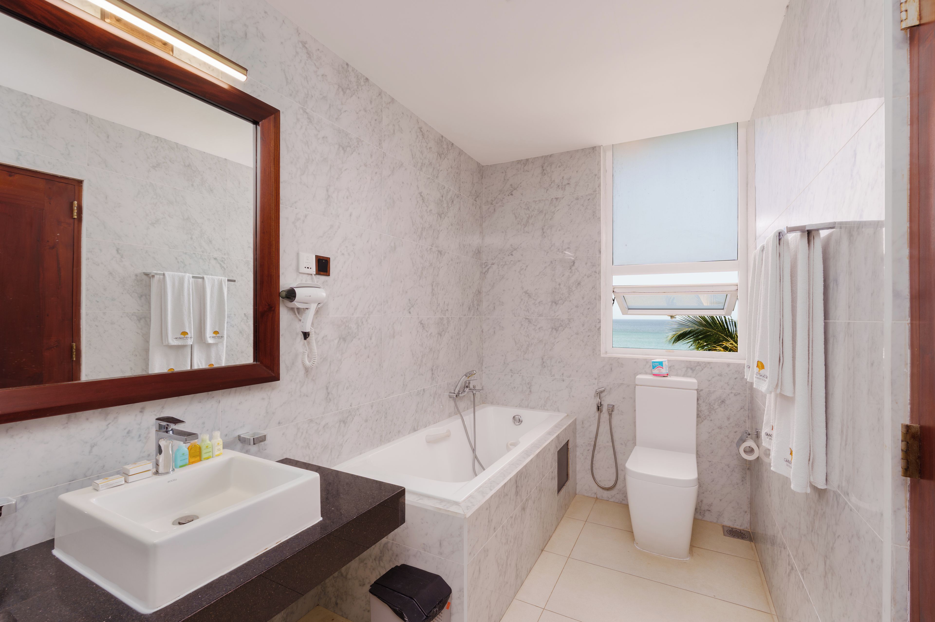 Un baño moderno con bañera, lavabo, espejo y ventana con vista al mar.
