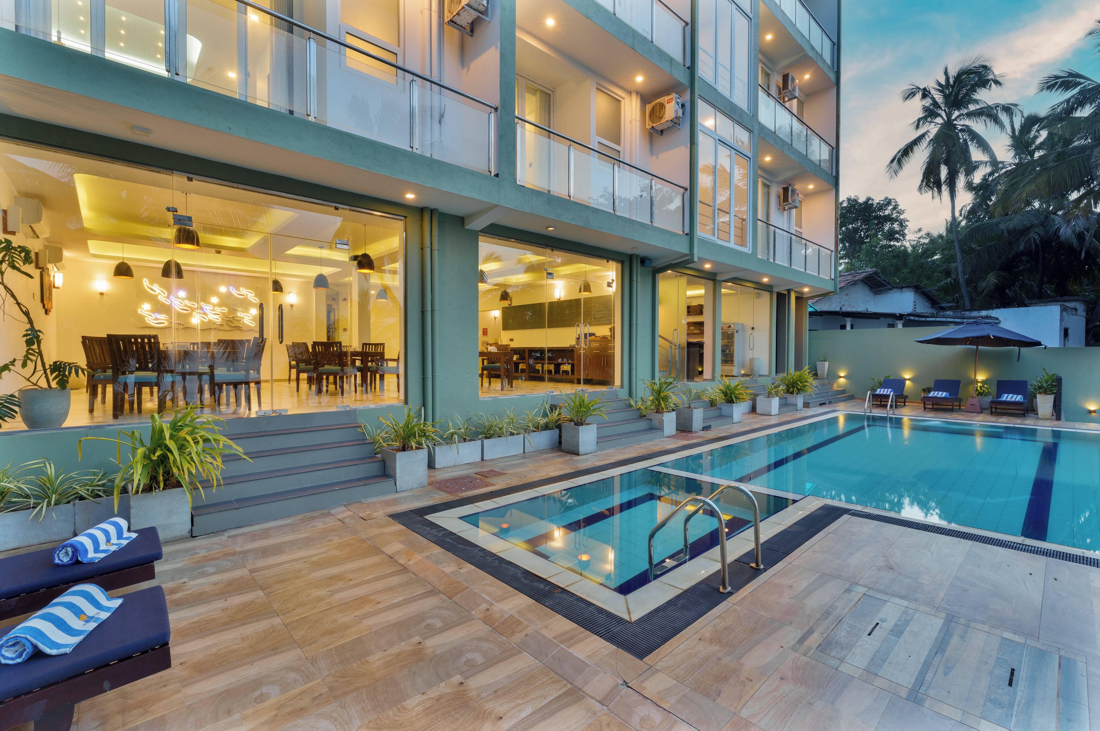 A modern hotel with a swimming pool, outdoor seating, and a well-lit interior.