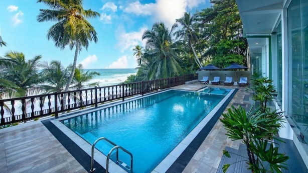 A swimming pool with a view of the ocean, surrounded by palm trees and lounge chairs. - Grand Samudra Hotel (Tangalle)