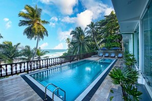 A swimming pool with a view of the ocean, surrounded by palm trees and lounge chairs.