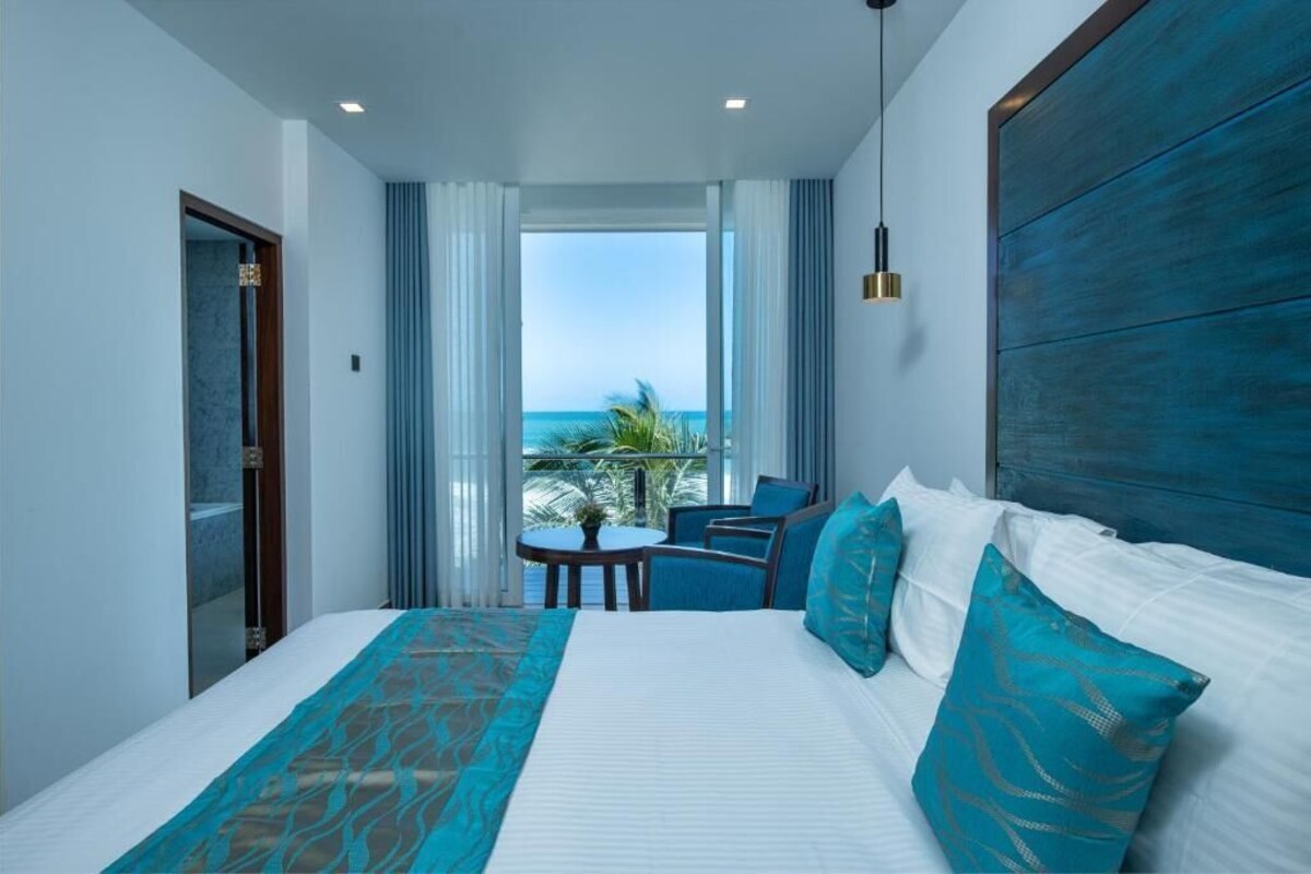 A hotel room with a bed, a seating area with a table, and a view of the sea.