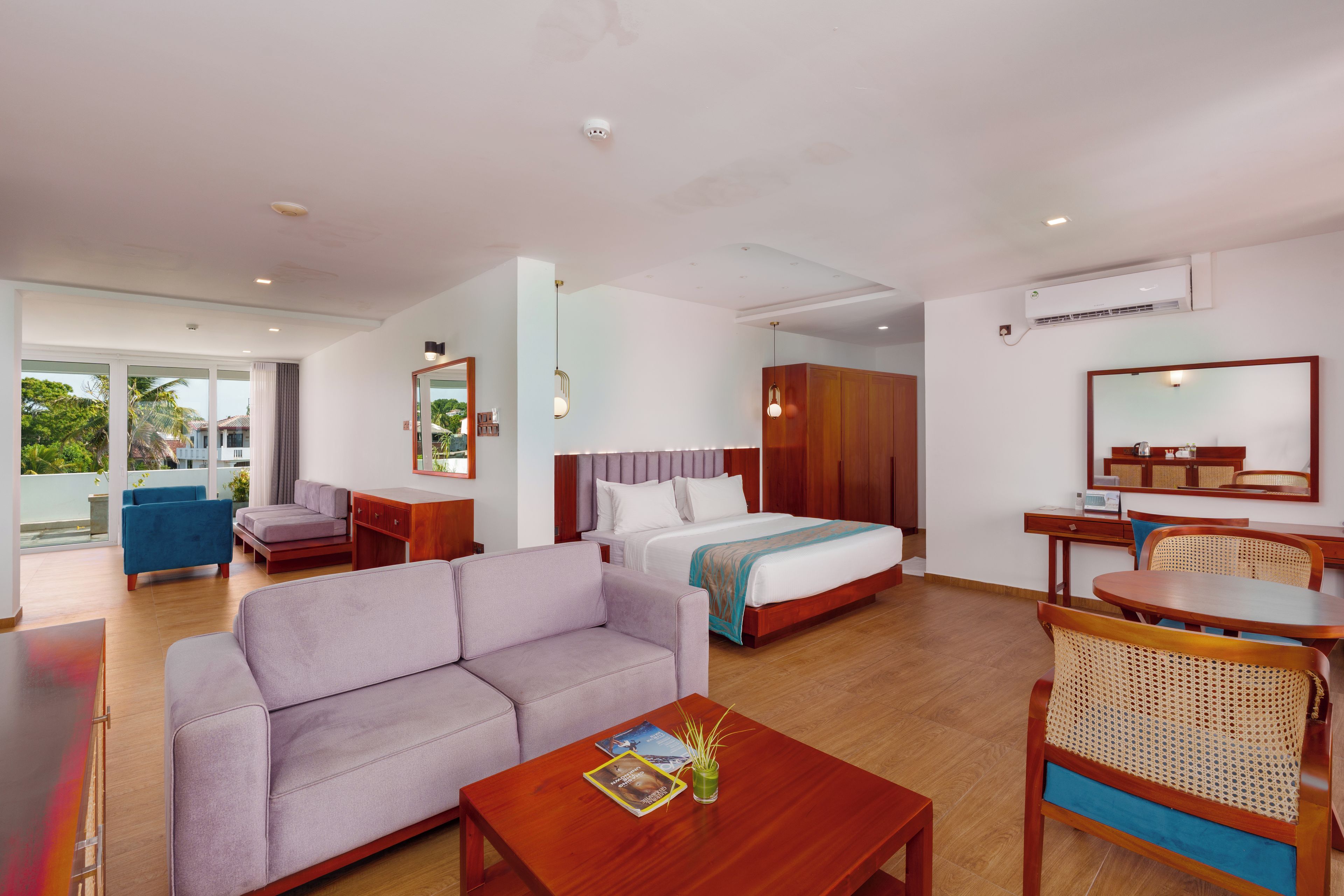 Habitación de hotel con cama, sofá, mesa de comedor y un pequeño balcón.