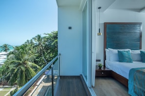 A balcony with a glass door leading to a bedroom with a bed, a nightstand, and a view of palm trees and the ocean.