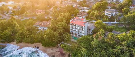 Vista aérea de una zona residencial costera con casas, una playa y palmeras.