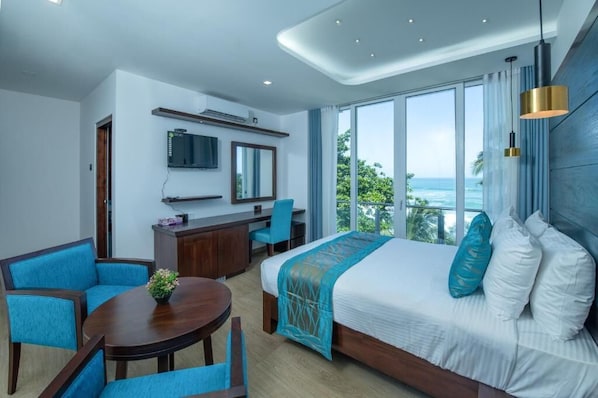 Habitación de hotel con cama, escritorio, silla, televisor y vista al océano.