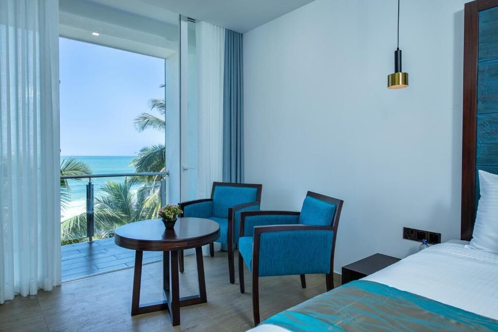 A hotel room with a bed, a table with chairs, and a view of the ocean.