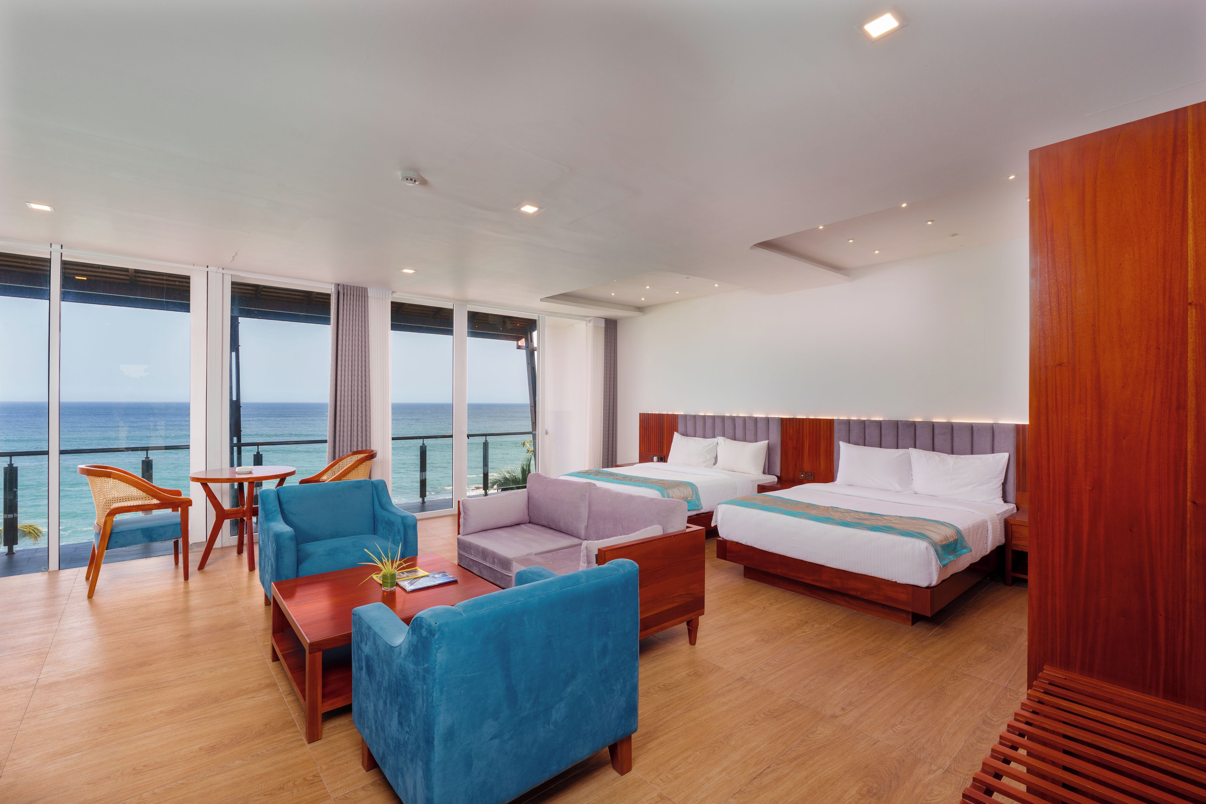 A hotel room with a large window, two beds, a seating area with chairs, and a wooden floor.