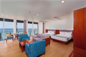 Habitación de hotel con un ventanal grande, dos camas, una zona de estar con sillas y suelo de madera.