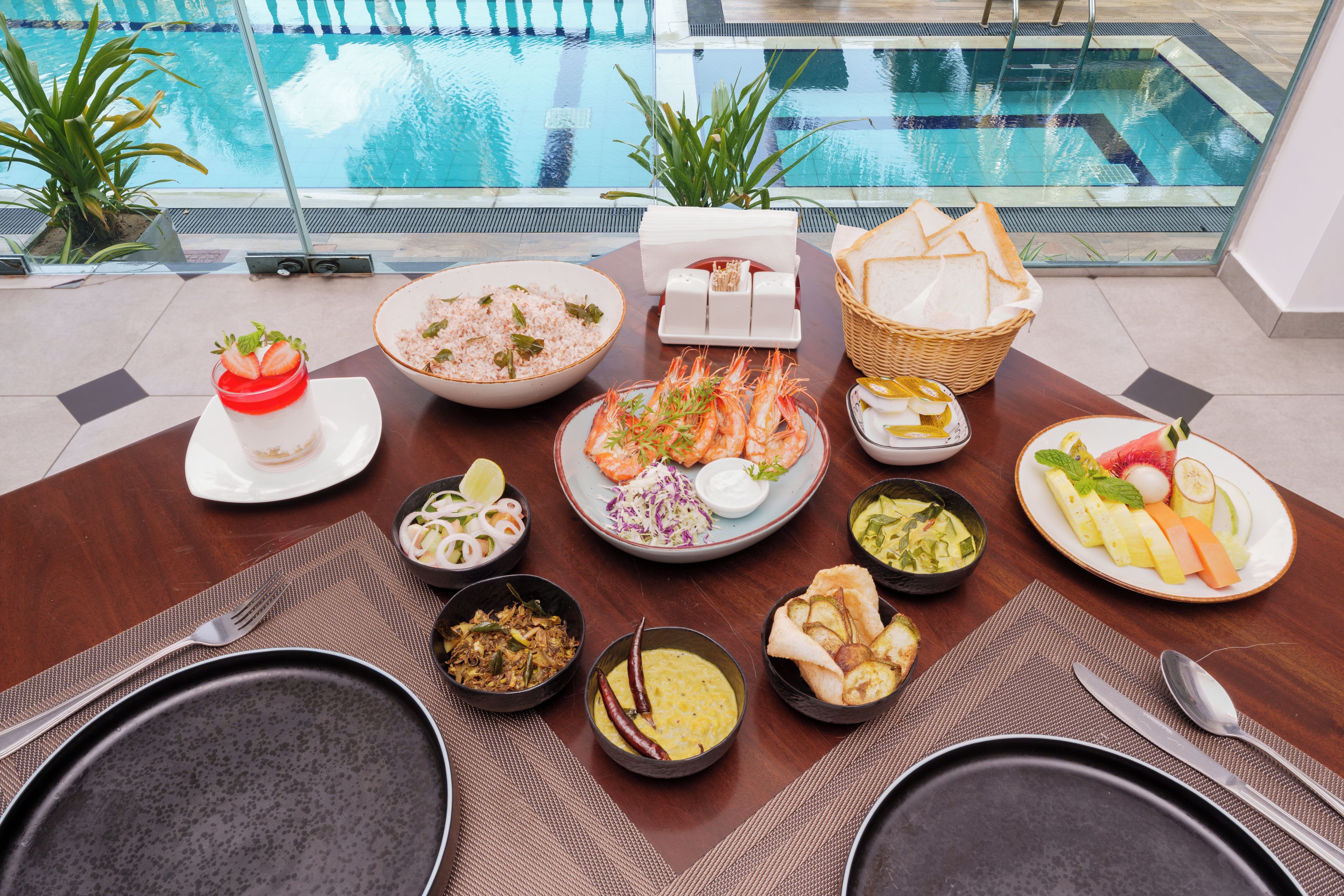 A dining table with various dishes, a glass of a red beverage, and a view of a swimming pool.