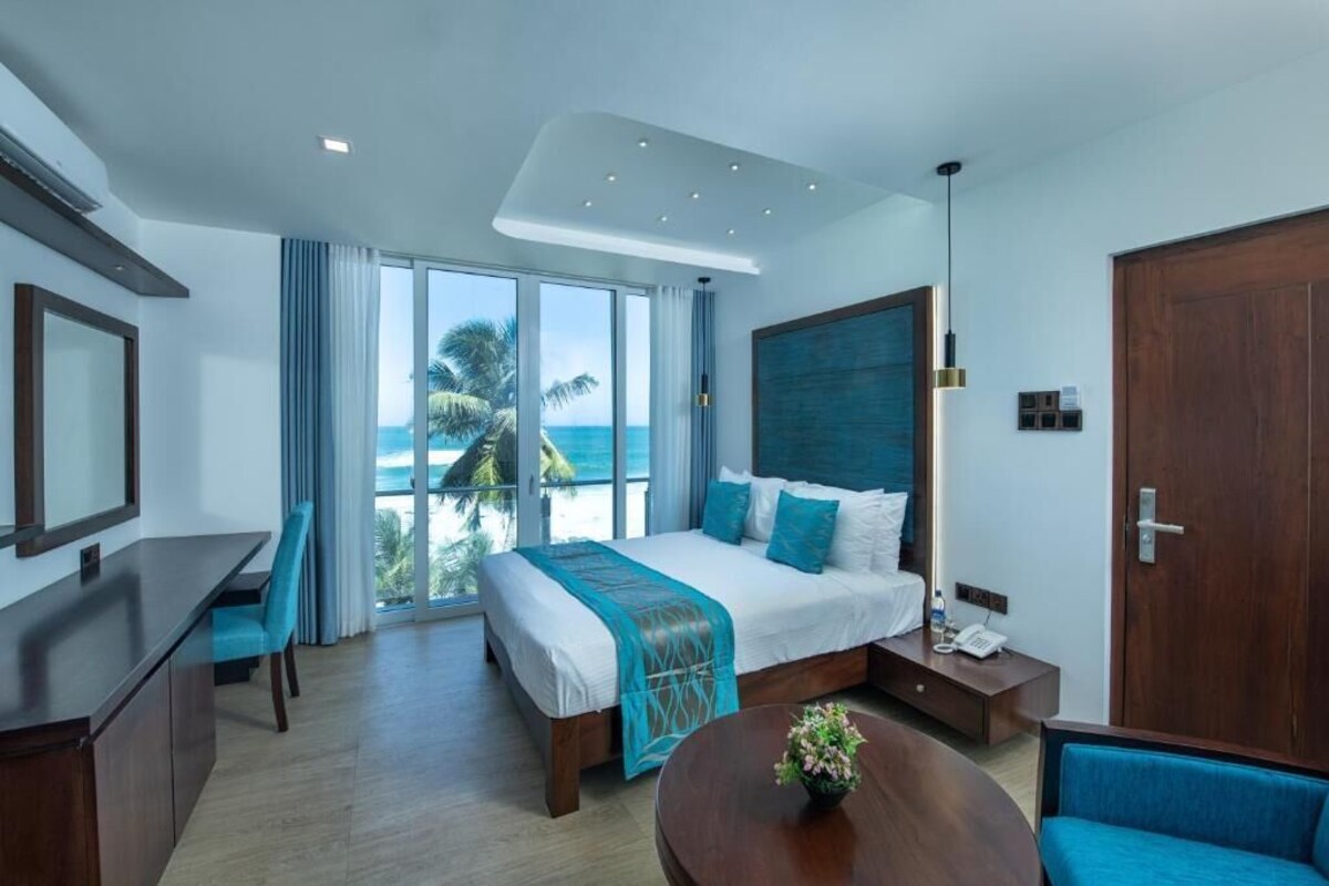 A modern hotel room with a large bed, a desk, a chair, a small table, and a view of the ocean.
