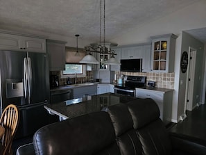 A modern kitchen with a central island, stainless steel appliances, and a dining area with leather seating. - Sage Lake Paradise (Hale)
