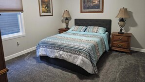 A bedroom with a bed, two nightstands, two lamps, a window with blinds, and two framed pictures on the wall. - Sage Lake Paradise (Hale)