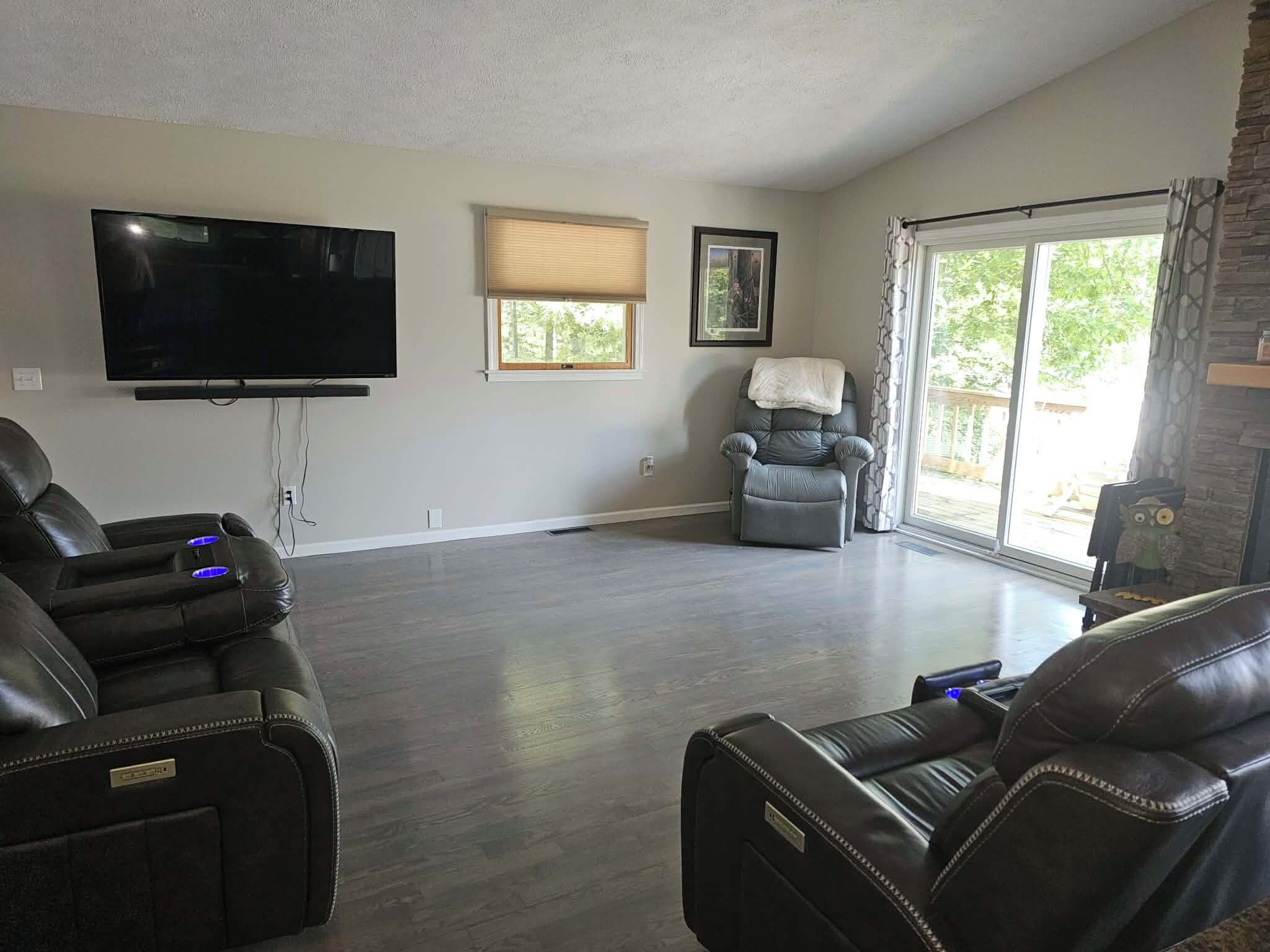 A spacious living room with a flat-screen TV, leather recliners, a fireplace, and a large window.
