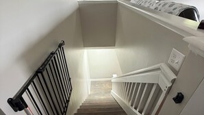 Una escalera con barandilla, un rellano con una lámpara y un televisor montado en la pared.