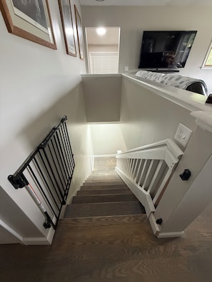 A staircase with a handrail, a landing with a light fixture, and a television mounted on the wall.