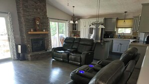 A spacious living room with a stone fireplace, leather recliners, and a kitchen area with white cabinets. - Sage Lake Paradise (Hale)