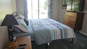 Una habitación de hotel con una cama, un escritorio con lámpara, un aparador y una televisión.