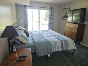 A hotel room with a bed, a desk with a lamp, a dresser, and a television.