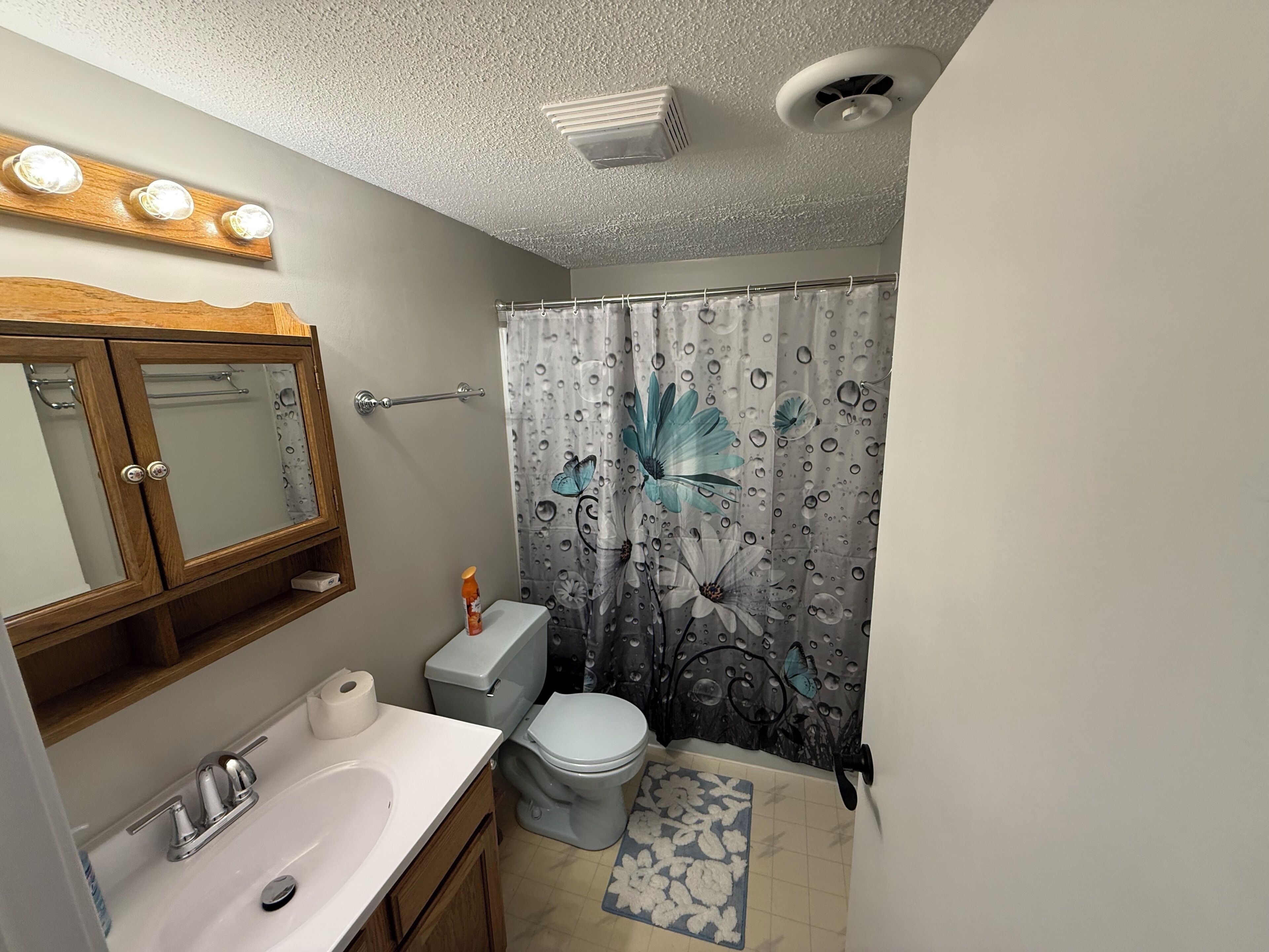 A bathroom with a wooden cabinet, a sink, a toilet, and a shower curtain with floral patterns.