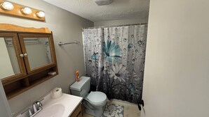 A bathroom with a wooden cabinet, a sink, a toilet, and a shower curtain with floral patterns. - Sage Lake Paradise (Hale)