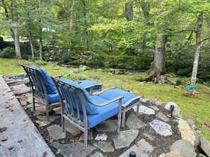 Espace extérieur aménagé avec des coussins bleus, un chemin en pierre et un décor naturel de forêt.