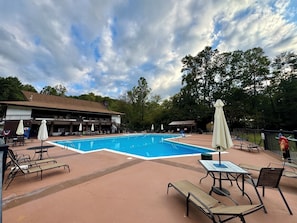 Une piscine entourée de chaises longues et de parasols, le tout bordé par un bâtiment doté d’une terrasse.