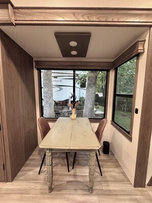 Een eethoek met een tafel, stoelen en uitzicht op een bebost gebied.