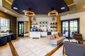 A spacious living area with a sofa, a coffee table, and a TV. There is a kitchen area with a sink, stove, and cabinets. The room has a tiled floor and a ceiling with recessed lighting. - Fort Myers 2BR Condo | Pool + BBQ + Gym (Fort Myers)