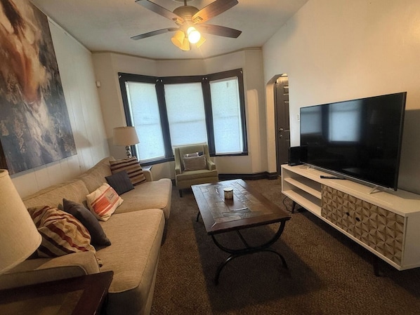 Ein Wohnzimmer mit einer Couch, einem Sessel, einem Couchtisch, einem Fernseher und einem Deckenventilator.