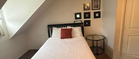 A bedroom with a bed, a small round table, a door, and a sloped ceiling with a skylight.
