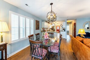 A dining area with a glass table, chairs, and a chandelier. - Charming 3-Bed Beach House with bathtub and BBQ (Surfside Beach)