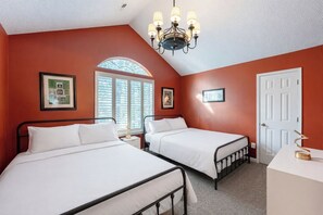 A bedroom with two beds, a chandelier, a white door, and a window with blinds. - Charming 3-Bed Beach House with bathtub and BBQ (Surfside Beach)