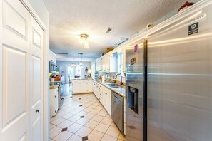 Une cuisine moderne avec des meubles blancs, un réfrigérateur en acier inoxydable et un sol carrelé.