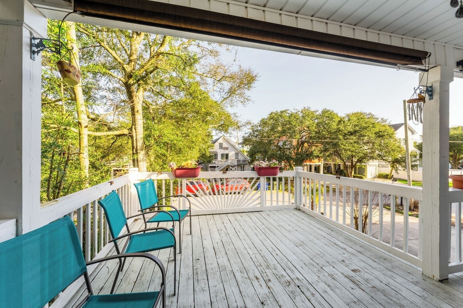 A wooden deck with chairs and potted plants, overlooking a residential street.