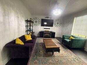 Ein Wohnzimmer mit einer Couch, einem Couchtisch, einem Fernseher, einer Kristallleuchtre und einem gemusterten Teppich.