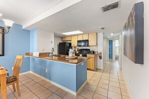 Uma cozinha moderna com paredes azuis, uma ilha central e uma área de refeições com mesa e cadeira de madeira.