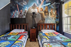 Quarto com duas camas, um mural com tema de Star Wars e uma janela com cortinas.