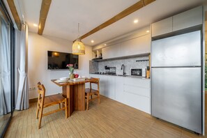 Una cocina moderna con mesa y sillas de madera, lámpara colgante y refrigerador empotrado.