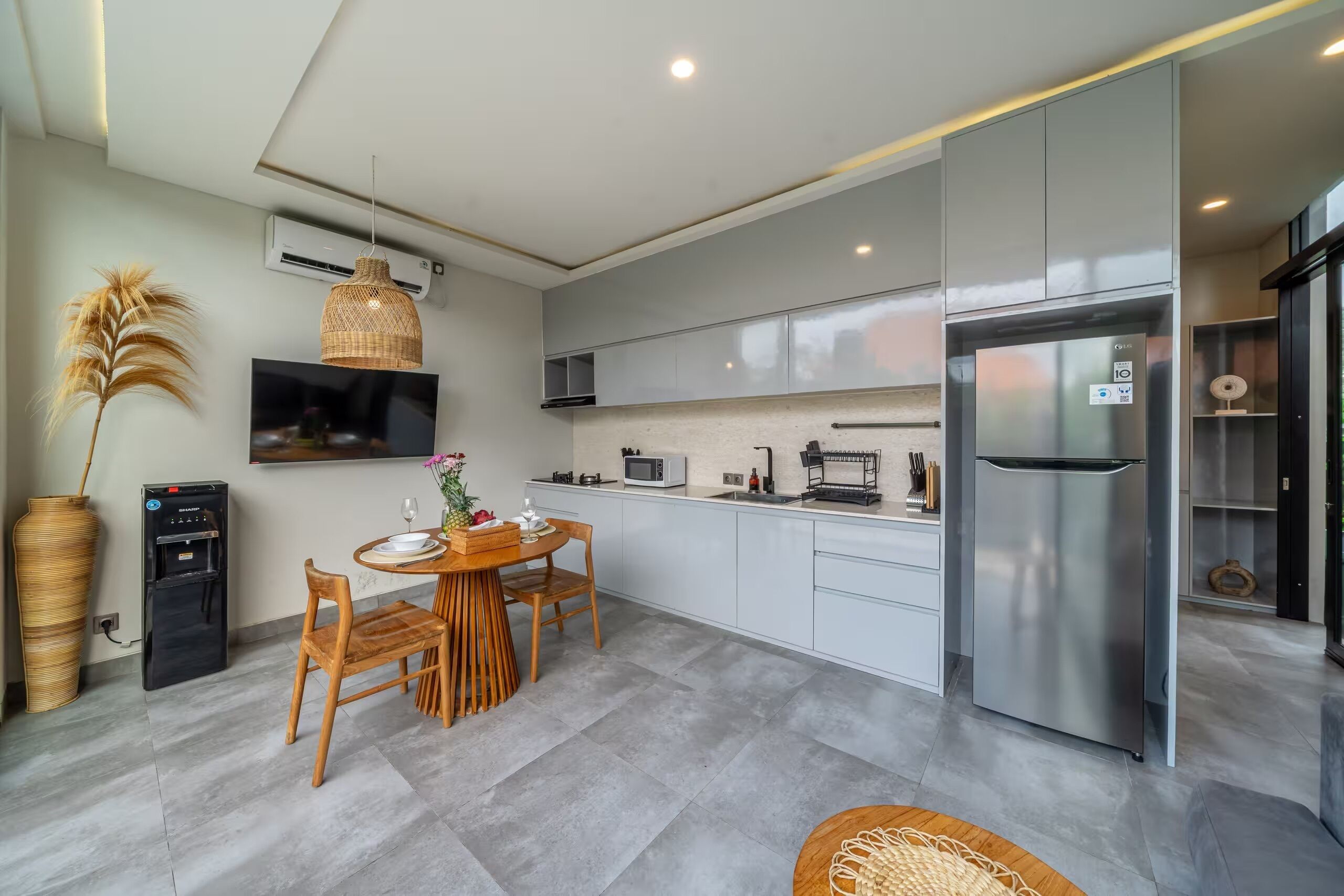 Una cocina moderna con armarios grises, un refrigerador de acero inoxidable, un microondas y un comedor con una mesa redonda y sillas.