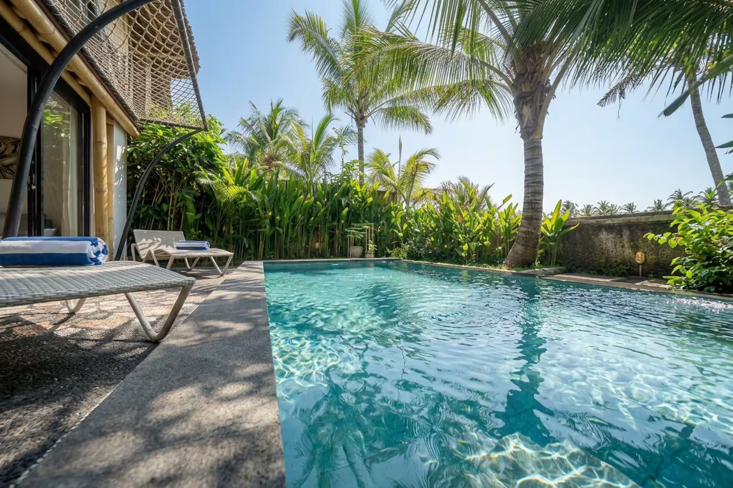 A clear swimming pool with lounge chairs and palm trees in the background.
