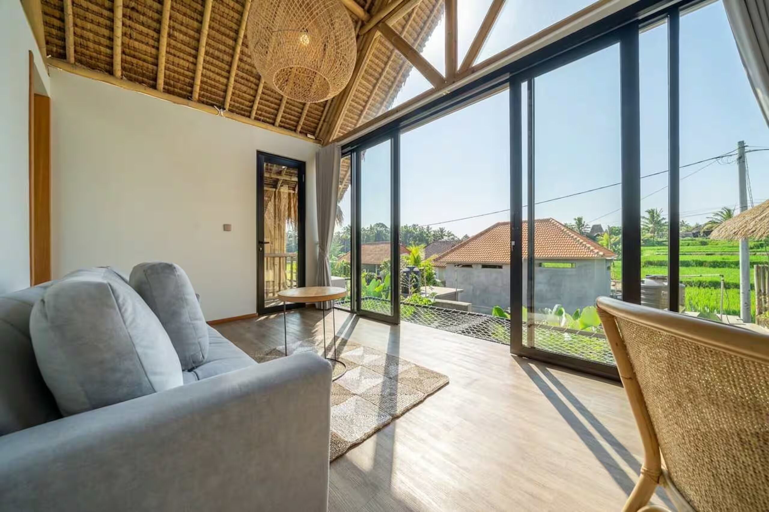 Una habitación con un ventanal grande, un sofá, una mesita pequeña y una silla de mimbre.