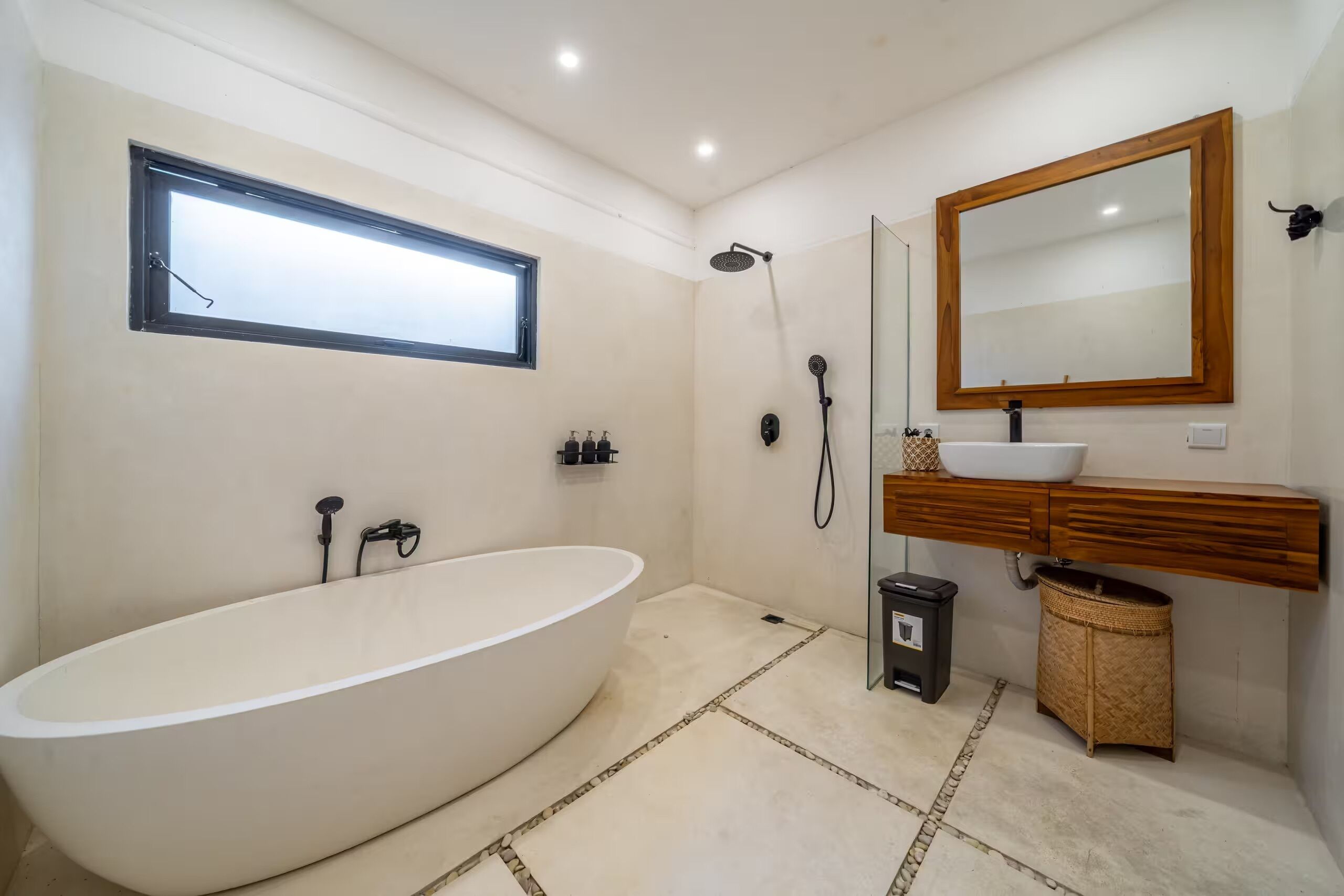 Un baño moderno con una bañera independiente, cabina de ducha de vidrio, tocador de madera y un espejo grande.