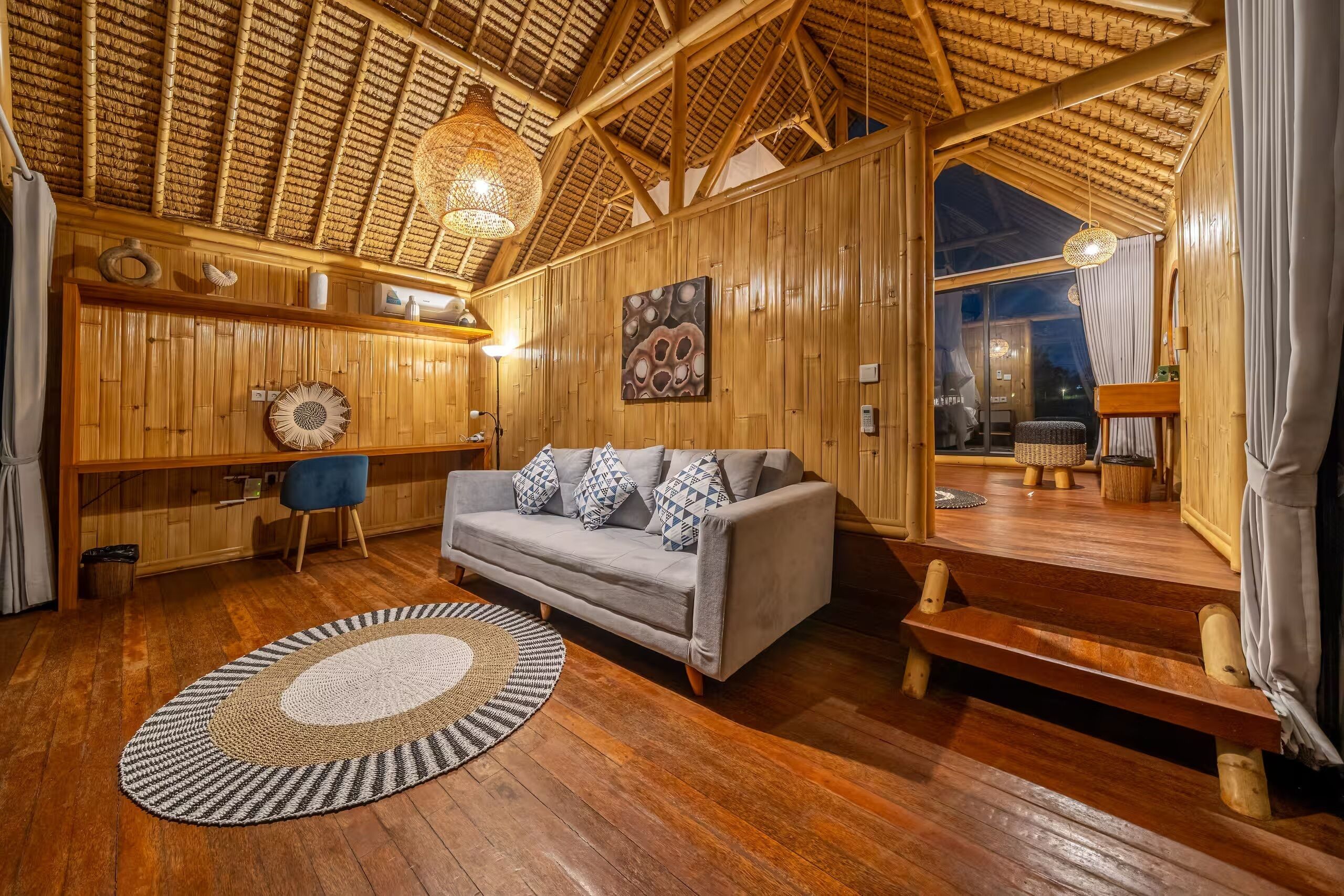 Una habitación acogedora con techo de madera, un sofá con cojines estampados, un tapete redondo y un ventanal grande.